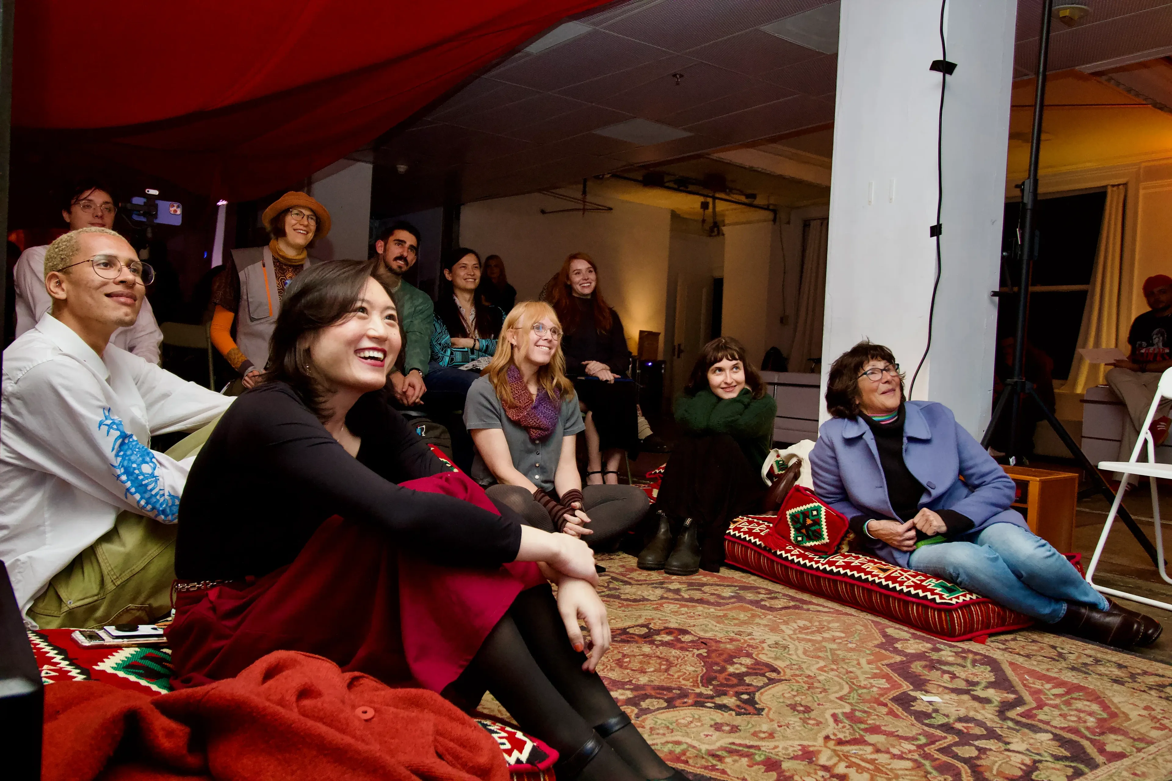 Dreamshare guests sitting together on rugs and floor cushions, laughing as they watch a talk