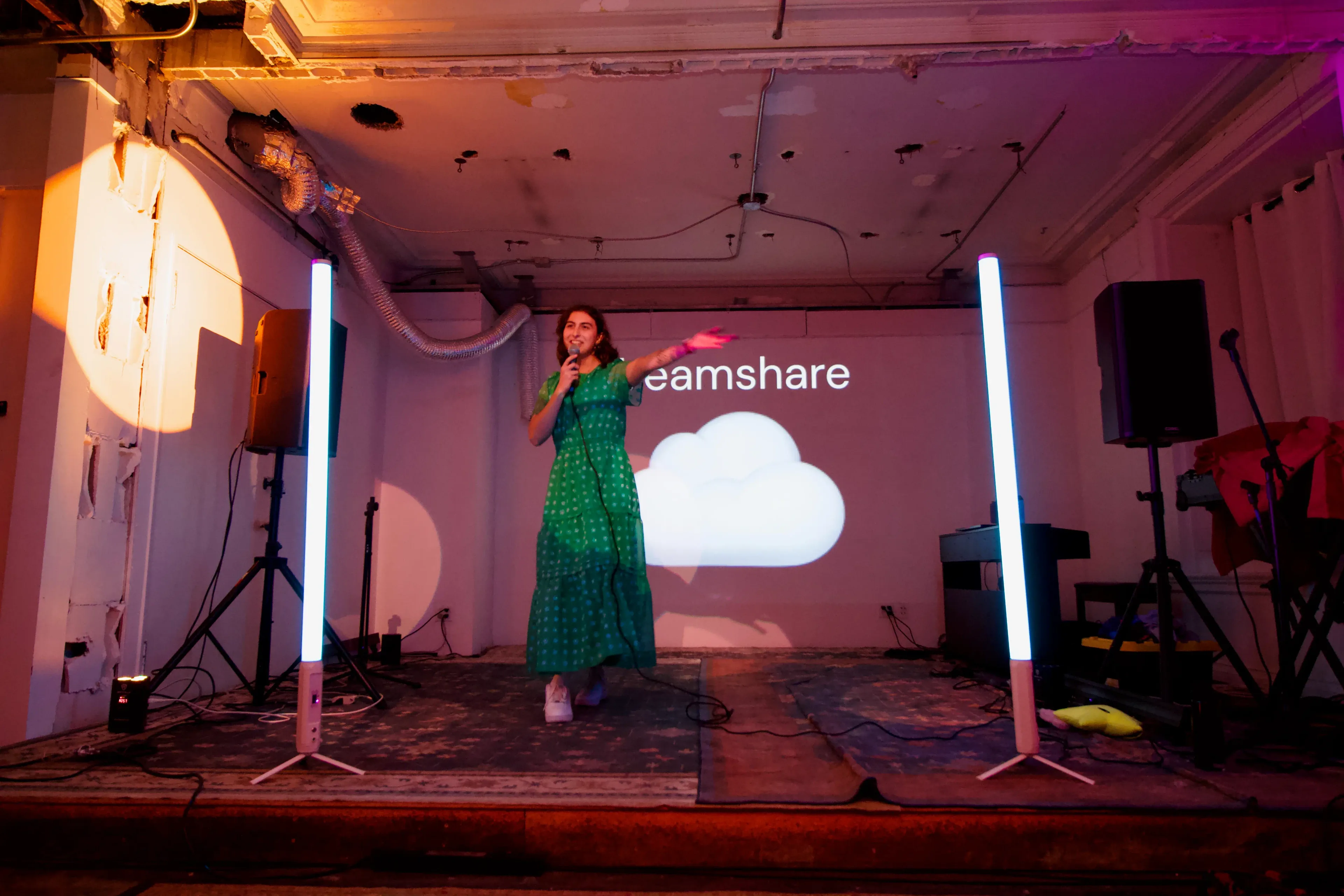 A speaker mid-talk on stage, the Dreamshare cloud projected on the wall behind her